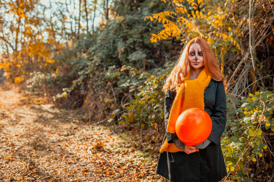 Woman with spooky make-up holding balloon while standing on footpath