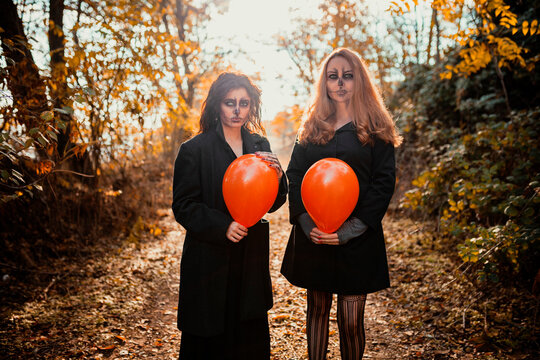 Friends with spooky make-up and costume holding balloon while standing on forest path