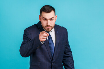 Serious bearded man wearing official style suit pointing finger, indicating direction to camera and...