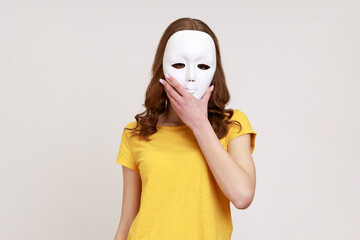 Unknown anonymous woman in yellow casual style t-shirt covering her face with white mask, hiding...