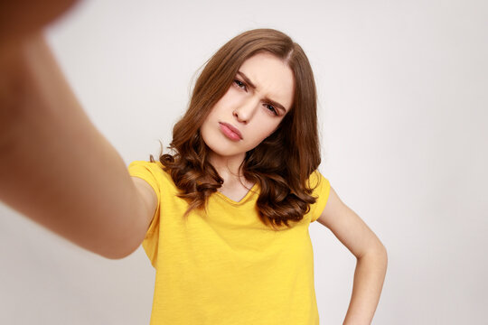 Confused beautiful teenager girl in yellow casual t-shirt looking at camera POV, point of view of photo, frowning face, misunderstanding expression. Indoor studio shot isolated on gray background.