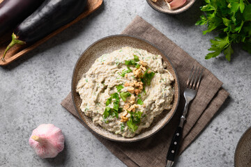 Baba ganoush appetizer from baked eggplant with fresh parsley, walnuts, garlic and olive oil on gray background. Arabic and lebanese cuisine. View from above.