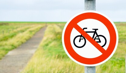 A round cycling prohibited traffic sign on a pole against a footpath and grass background with copy space