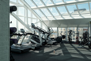Horizontal no people wide shot of various exercise machines in modern gym with panoramic windows in daylight