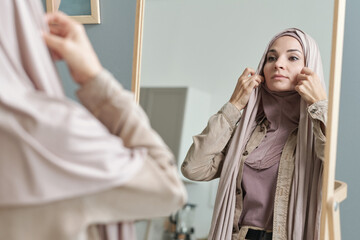 Horizontal over-the-shoulder shot of attractive young adult Muslim woman getting ready to go out...
