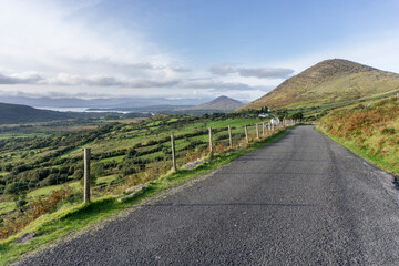 narrow road with asphalt and green grass through hills and valley on the wild Atlantic way in ireland with no cars on it