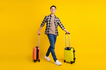 Photo of traveler guy carry two suitcase stroll wear plaid shirt jeans footwear isolated yellow...