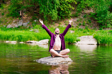 Meditation and peace. A man meditates in the lotus position, sitting on a stone in the middle of a mountain river..