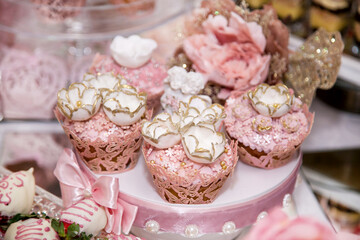 Obraz na płótnie Canvas Delicious desserts at the wedding candy bar in the buffet area: muffins decorated with angels, sugar rosebuds and gold dye