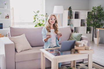 Photo of smiling businesswoman in glasses hold carton boxes working remote from house manager marketer use laptop