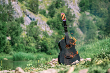 Bonfire from the guitar. Black acoustic guitar on fire on the background of the forest and the...