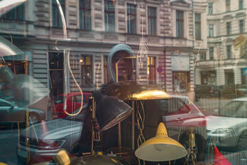 The reflection of a young man in a shop window with old lamps