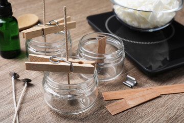 Glass jars with wicks and clothespins as stabilizers on wooden table. Making homemade candles - obrazy, fototapety, plakaty