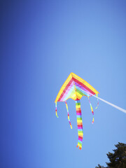 Multicolored kite in LGBT like colors attached to a white string against blue sky from festival in Latvia