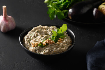 Baba ganoush Asian cuisine appetizer made from baked eggplant with parsley, garlic and olive oil on black table. Close up. Middle Eastern cuisine, vegan hummus.
