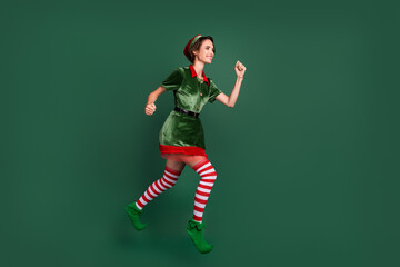 Fototapeta na wymiar Profile photo of active cheerful lady jump run wear elf costume hat striped stockings isolated green color background