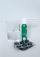 Medicines, tablets and spray with a glass of water on a light background