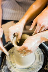 Pottery making. Smeared in clay hands of man and woman on potter's wheel. A couple is making a vessel or a bowl or a vase