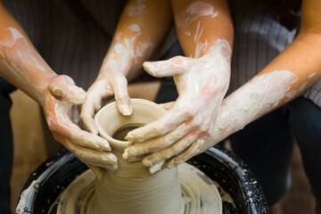 Pottery making. Smeared in clay hands of man and woman on potter's wheel. A couple is making a vessel or a bowl or a vase