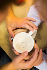 White clay cup with drawn heart inside with hands of man and woman
