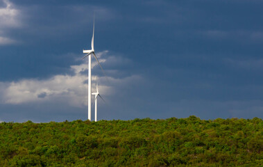 Two white windmills on a green hill, sky background