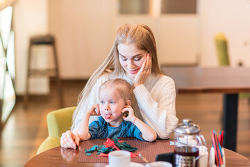 Mom with a naughty child in a cafe. The girl shows her - obrazy, fototapety, plakaty
