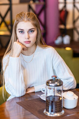 A girl with a white blouse drinks coffee in a cafe.