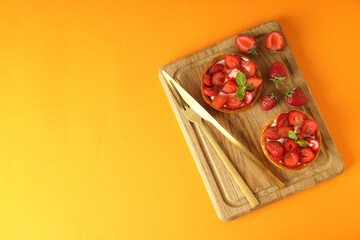 Board with strawberry tarts on orange background