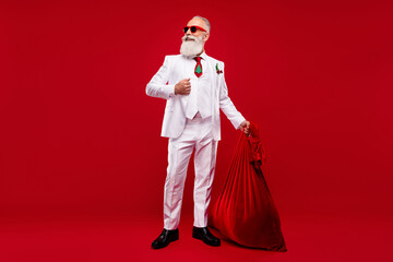 Full length photo of happy dreamy old man look empty space hold bag santa claus isolated on red color background