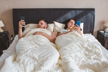couple laying in bed surfing internet on phone