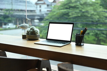 Photo of a wooden counter surrounded by a white blank screen laptop computer and various accessories, Cozy workplace concept.