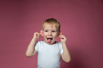 Caucasian boy makes faces, shows tongue, looking at camera on pink background
