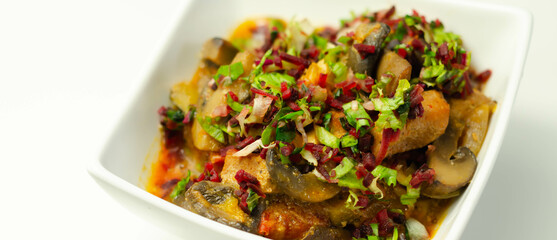 A thick stew of meat, potatoes, mushrooms, and mix of peppers served in a white bowl