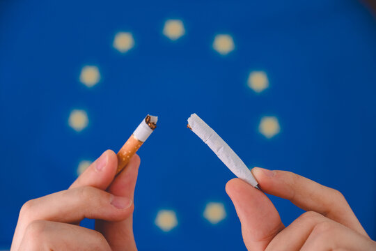 Hand breaks a cigarette in the background of the EU flag.