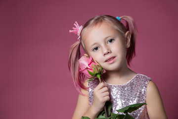 Little caucasian girl in a festive dress with sequins posing with rose flower