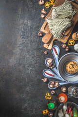 Food background with asian food ingredients: ramen noodles, shiitake, rice cakes, chili pepper and asian crockery. Dark grey concrete kitchen table. Top view with copy space. Vertical border