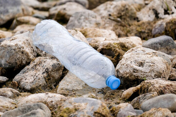 Plastic bottle among the stones. Garbage on the river bank. No one