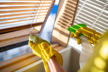 Professional cleaning of apartments and houses. Cleaning service in work clothes and rubber gloves washes the blinds. Wiping dust from a window