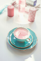 Turquoise porcelain cup with pink flowers tea on light table with candles and cosmetics. Female...