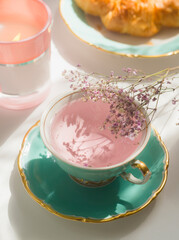 Close up of pink flowers tea in turquoise teacup on sunny breakfast table