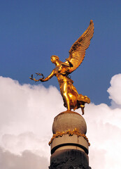 Fototapeta premium Golden Sculpture Of A Young Woman With Wings In Reims In France On A Beautiful Spring Day With Some Clouds In The Blue Sky