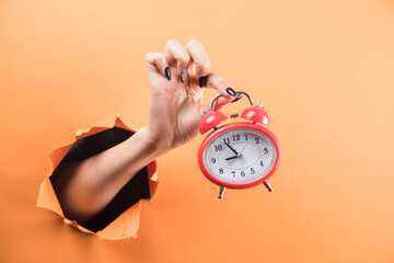 female hand holding alarm clock on orange background