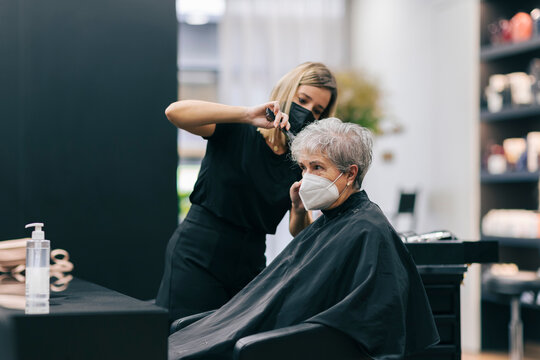 Female hairdresser cutting hair of customer in salon during COVID-19