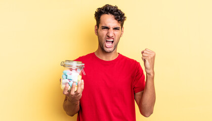 hispanic handsome man shouting aggressively with an angry expression. candies concept
