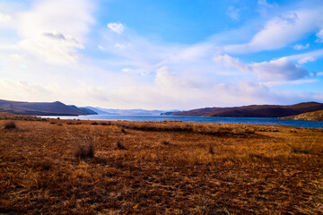 Nature landscape with golden field, wather, hills and blue sky with white clouds in a day or a evening
