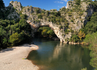 Fototapeta na wymiar Rock Arch Pont D'Arc In The Canyon Of The Gorges De L'Ardeche With Reflections On The River Ardeche In France On A Beautiful Autumn Day With A Clear Blue Sky