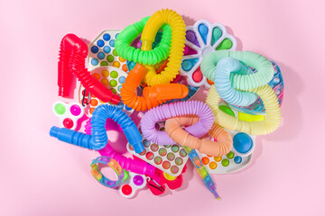 Modern trendy kids fidget finger toys, relaxation concept - set of different bright pop-it, simple-dimple, squishy, pop-tubes, on colorful pink background, top view copy space