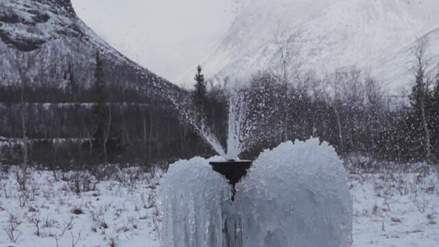 Water gushes (leaky cap) from an artesian well enclosed in a pipe (bored tube well) in the middle of a mountainous area. Winter and freezing of ice and snow on the bush .Super slow motion 1000 fps.