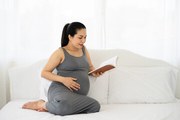 pregnant mom reading book with baby and touching her belly resting in bedroom. pregnancy, people and motherhood concept