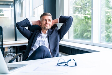 Thoughtful businessman with hands behind head relaxing in office